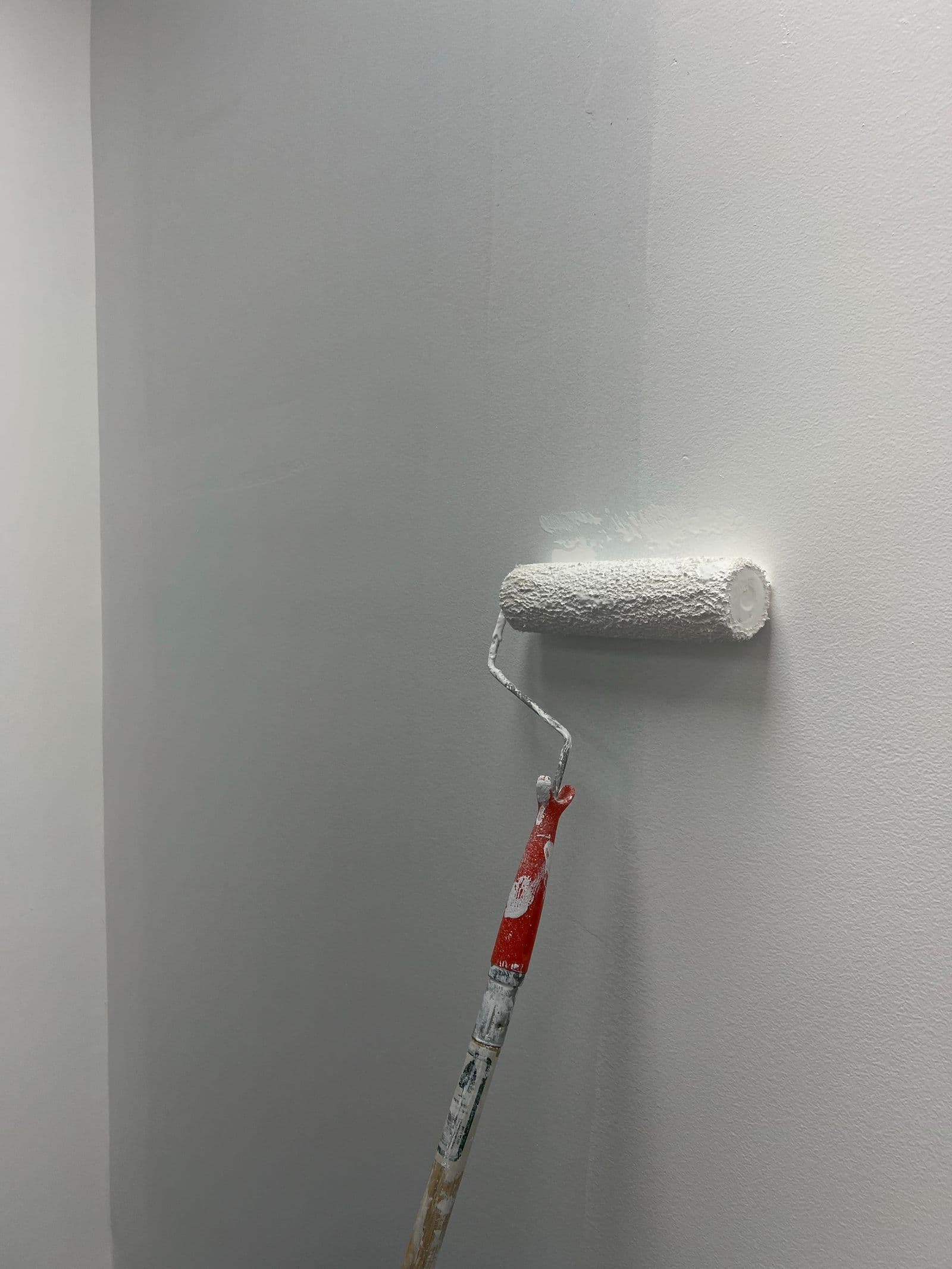 Málningarrúlla ber ferska hvíta málningu á sléttan vegg í björtu rými.